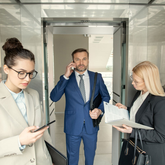 Biznesowo ubrani ludzie w windzie, ilustracja do artykułu o powitaniach w windzie